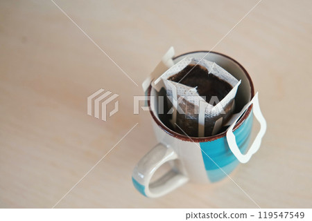 Drip bag fresh coffee. Pouring hot water into blue cup with drip coffee bag. Instant freshly brewed cup of ground coffee. Coffee Trend. Quick way to brew using paper filter. The process of brewing Drip bag fresh coffee. Pouring hot water into blue cup with drip coffee bag. Instant freshly brewed cup of ground coffee. Coffee Trend. Quick way to brew using paper filter. The process of brewing 119547549