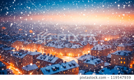 Winter evening cityscape, snowfall over residential area, warm lights glow from windows, cozy urban scene 119547939
