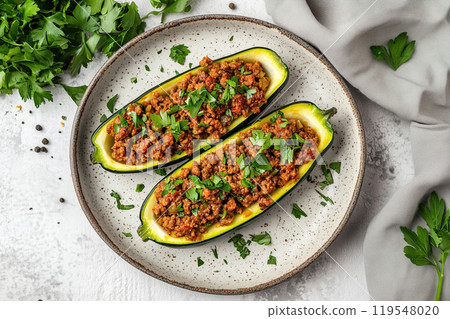 Delicious stuffed zucchini boats topped with fresh herbs, served on a plate with a light gray cloth 119548020