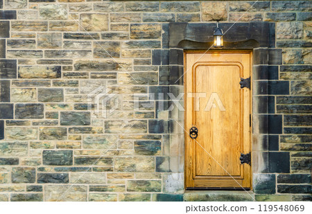 Wooden door with knocker and stone wall with lantern hangs above door 119548069