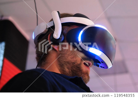 Man wearing VR Glasses. Surprised adult male having fun play VR headset virtual reality goggle, 3D cyber space. Neon blue red UV lighting. Digital technology, game Man wearing VR Glasses. Surprised adult male having fun play VR headset virtual reality goggle, 3D cyber space. Neon blue red UV lighting. Digital technology, game 119548355
