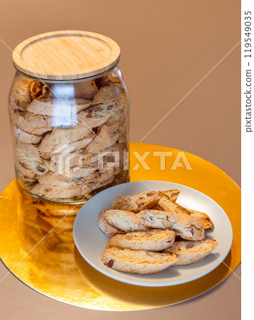 Almond cantucci cookies rest on a white plate next to a glass jar with a wooden lid Almond cantucci cookies rest on a white plate next to a glass jar with a wooden lid 119549035