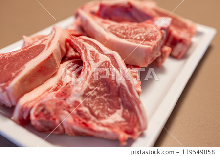 Several raw lamb chops on white plate show marbled pink meat and visible fat ready for cooking 119549058