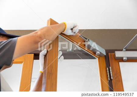 Handyman fixing door closer and adjust  hydraulic arm extended. 119549537