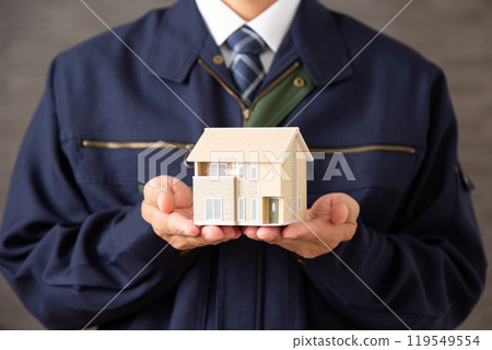 Middle-aged male businessman wearing work clothes holding a house model 119549554