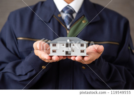 Middle-aged male businessman wearing work clothes holding a model of an apartment building 119549555