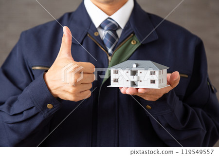 A middle-aged male businessman wearing work clothes making a fist pump while holding a model of an apartment building A middle-aged male businessman wearing work clothes making a fist pump while holding a model of an apartment building 119549557