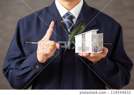 一位穿著工作服的中年男性商人拿著房屋模型，用食指指著 119549832