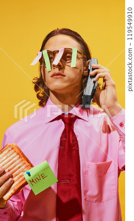 Man holding sandwich labeled MINE while on phone, sticky notes on his glasses against vibrant yellow background. 119549910