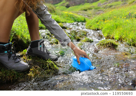 Hiker filling canrteen in a creek in the mountain Hiker filling canrteen in a creek in the mountain 119550693