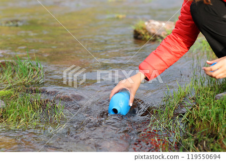 Hiker filling canteen with river raw water Hiker filling canteen with river raw water 119550694