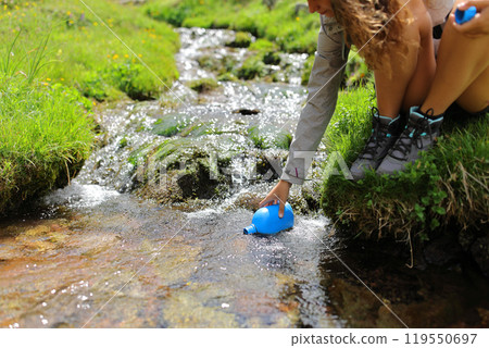 Hiker hand filling canteen of raw water in a creek Hiker hand filling canteen of raw water in a creek 119550697