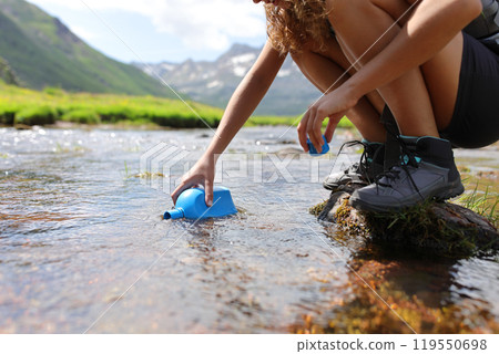 Hiker hand filling canteen of raw water in a river 119550698
