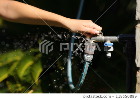 Woman hand opening hose faucet with water leak in a garden 119550889