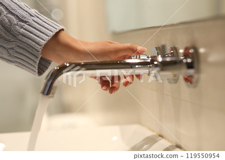 Woman hand opening faucet in a bathroom Woman hand opening faucet in a bathroom 119550954