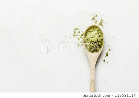 Green powder sits in a wooden spoon against a light background, highlighting its texture and color Green powder sits in a wooden spoon against a light background, highlighting its texture and color 119551117