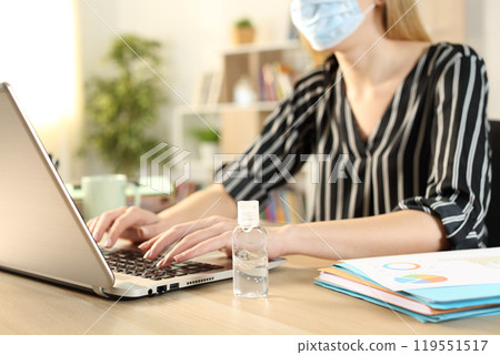 Entrepreneur with mask and hand sanitizer typing on laptop Entrepreneur with mask and hand sanitizer typing on laptop 119551517