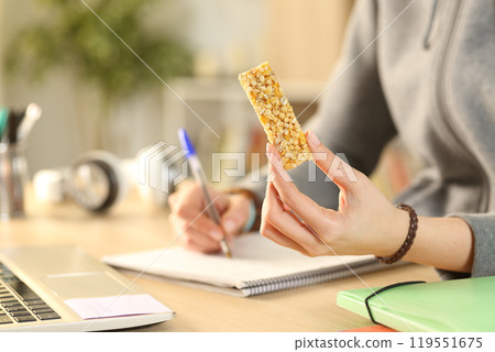 Student hands holding cereal snack bar studying Student hands holding cereal snack bar studying 119551675