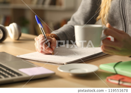 Student hands holding coffee cup writing at night Student hands holding coffee cup writing at night 119551678