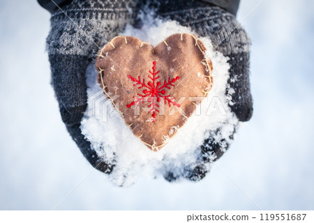 Hands in gloves holding a handmade heart ornament with a snowflake embroidery Hands in gloves holding a handmade heart ornament with a snowflake embroidery 119551687