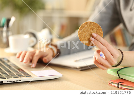 Student studying using laptop holding cookie at home 119551776