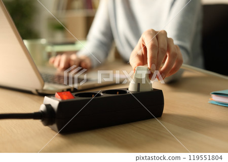 Woman hand plugging plug on socket at night using laptop 119551804