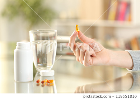 Woman hand showing omega vitamin pill at home Woman hand showing omega vitamin pill at home 119551810