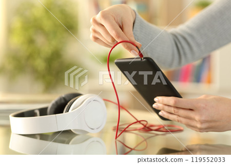 Woman hands plugging headphones to smart phone Woman hands plugging headphones to smart phone 119552033
