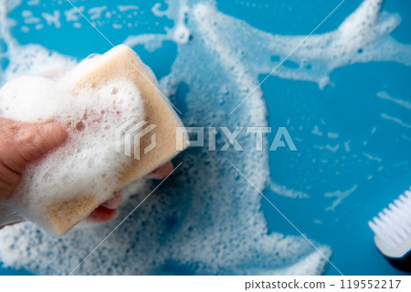 Hand holds a cleaning sponge and wipes a soapy foam on a blue tile. 119552217