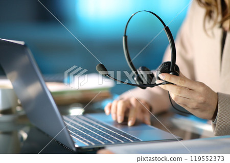 Tele marketer holding headset using laptop at homeoffice Tele marketer holding headset using laptop at homeoffice 119552373