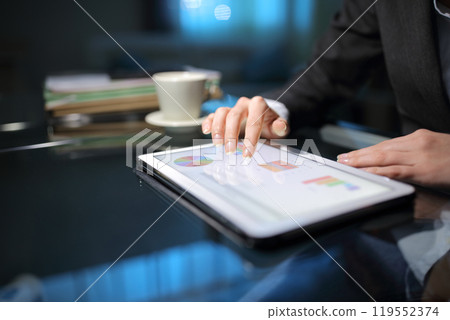 Tele worker checking graphs on a tablet late hours 119552374