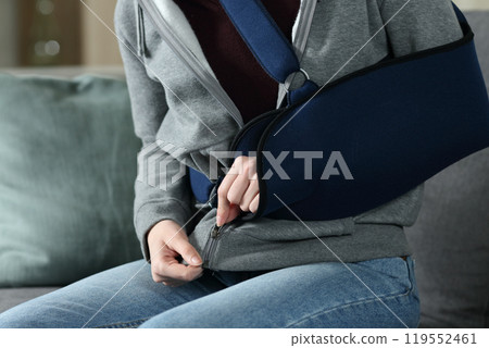 Woman with broken arm and sling trying to fastening zipper Woman with broken arm and sling trying to fastening zipper 119552461