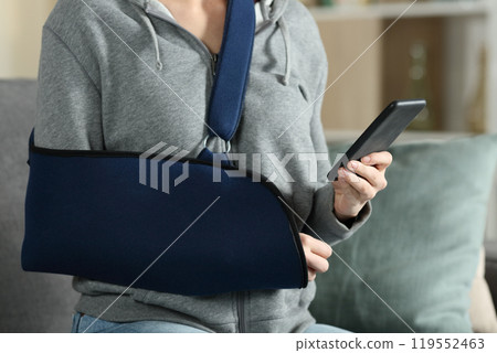 Woman with broken arm wearing sling using smart phone 119552463