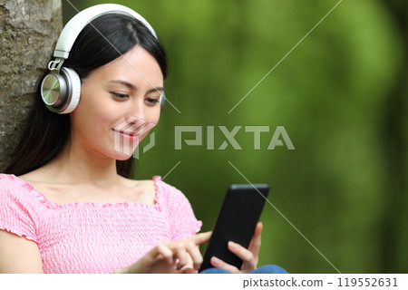Asian woman listening to music checking smart phone Asian woman listening to music checking smart phone 119552631