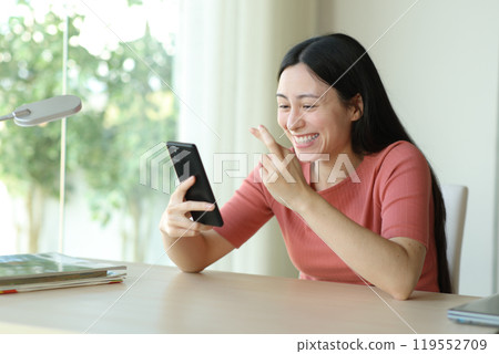 Happy asian woman crossing fingers checking phone in a desk Happy asian woman crossing fingers checking phone in a desk 119552709