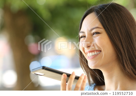 Happy asian woman dictating message on phone outdoors Happy asian woman dictating message on phone outdoors 119552710