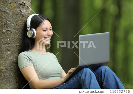 Happy asian woman watching media on laptop in a park 119552756