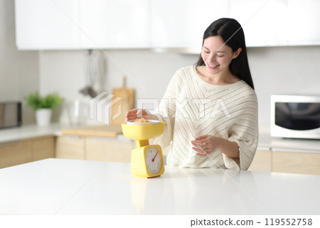 Happy asian woman weighing cereals standing in the kitchen 119552758