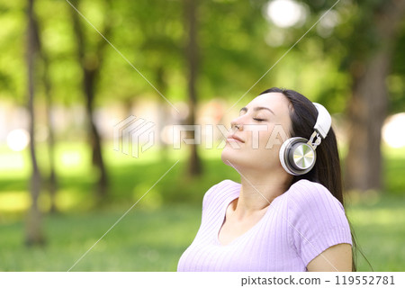 Relaxed asian woman listening to music in a park Relaxed asian woman listening to music in a park 119552781