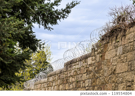 Barbed wire fence on high wall perimeter for security and protection 119554804