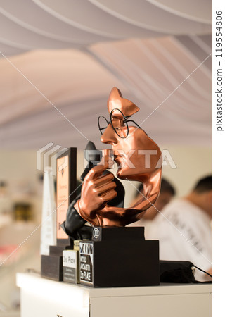A bronze sculpture of a man's face with glasses sniffing a small bottle. A bronze sculpture of a man's face with glasses sniffing a small bottle. 119554806