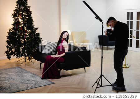 A beautiful woman in a shiny dress with a microphone at the Christmas tree singing song and recording video. The singer's performance at the New Year's holiday A beautiful woman in a shiny dress with a microphone at the Christmas tree singing song and recording video. The singer's performance at the New Year's holiday 119555359