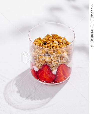 Glass filled with yogurt, granola and strawberries is standing on white surface 119555690