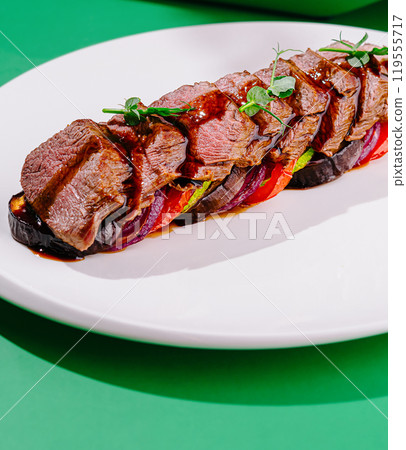 Grilled beef with vegetables and sauce on white plate on green background Grilled beef with vegetables and sauce on white plate on green background 119555717