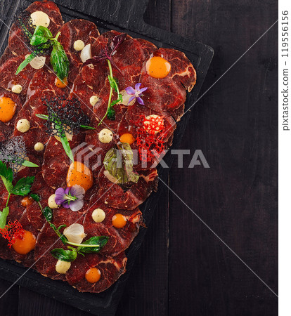 Exquisite beef carpaccio with edible flowers and garnishes on dark wooden background Exquisite beef carpaccio with edible flowers and garnishes on dark wooden background 119556156