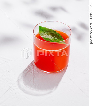 Glass of freshly squeezed tomato juice with basil leaf on white table 119556173