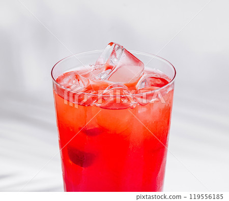 Red cocktail standing on white cube with palm leaf shadow 119556185