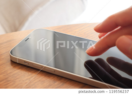 A woman's hand operating a smartphone at a table 119556237