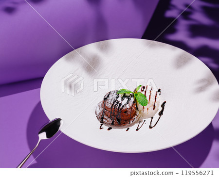 Chocolate fondant with vanilla ice cream decorated with mint leaves on white plate on purple background 119556271