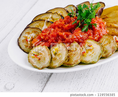 Grilled eggplant and zucchini slices lying on plate with tomato salsa and parsley Grilled eggplant and zucchini slices lying on plate with tomato salsa and parsley 119556385